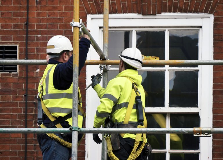 Two men applying scaffolding to house.