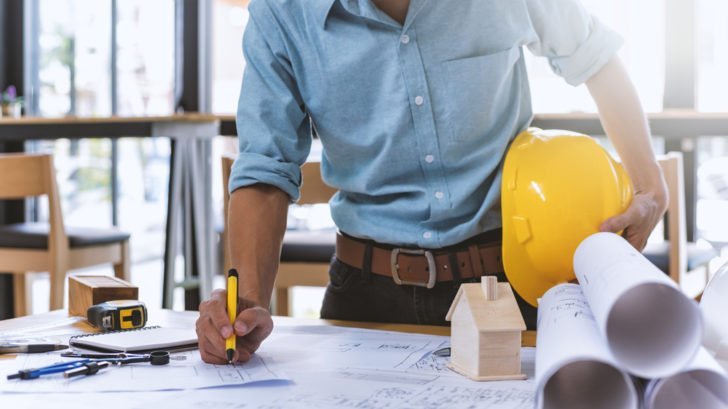 man writing on architectural drawing