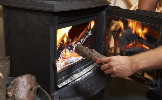 Man,Putting,Log,Onto,Wood,Burning,Stove